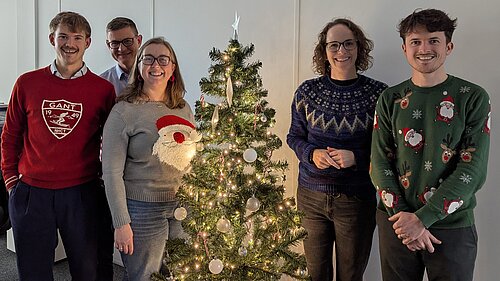 Alison Bennett MP and Team next to their office Christmas tree, while wearing Christmas jumpers